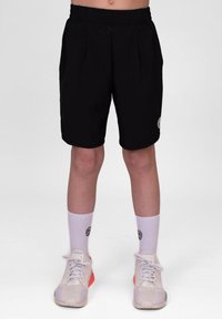 Schwarze Sportshorts mit einem elastischen Bund, seitlichen Taschen und einem Logo-Patch. Getragen mit weißen Socken und hellen Turnschuhen.
