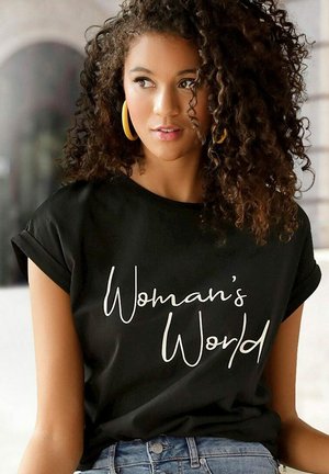 T-shirt nera a maniche corte con la scritta "Woman's World" in testo corsivo bianco. Tessuto morbido, vestibilità comoda, abbinata a pantaloni in denim blu.