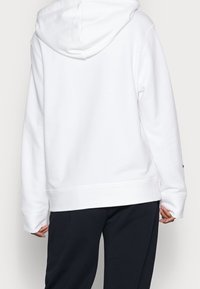Biała bluza z kapturem i sz nurkami, luźny krój, ściągacze przy mankietach i u dołu. Noszona na ciemne spodnie, charakteryzujące się gładką teksturą materiału.