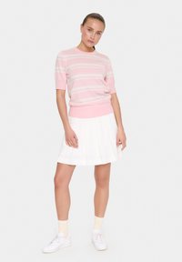 Suéter de punto rosa claro con rayas blancas, de mangas cortas y con un dobladillo acanalado, combinado con una falda blanca plisada y zapatillas blancas.