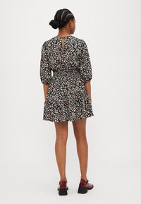 Blomstret kort kjole i sort, med puffede ærmer, elastisk talje og nøglehul bagpå. Pynter med små, flerfarvede blomster.