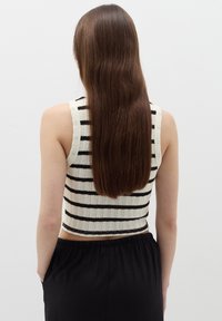 Top senza maniche all'uncinetto di colore crema con righe orizzontali nere, caratterizzato da un design cropped e un knit texturizzato. Abbinato a una gonna nera.