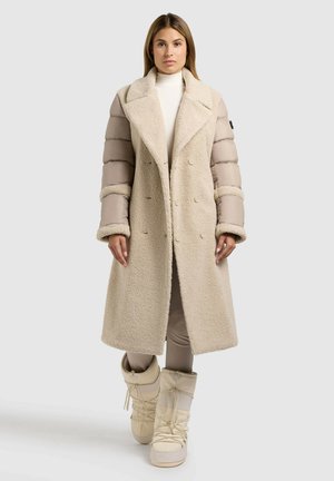 Beige dobbeltrækket frakke med struktureret yderlag, polstrede ærmer og brede klap. Sammen med cremefarvede isolerede støvler.