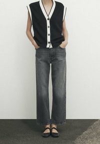 Svart ärmlös topp med vit kant och knappar, kombinerad med högmidjade, raka ljusgrå jeans. Avslutad med svarta flats.