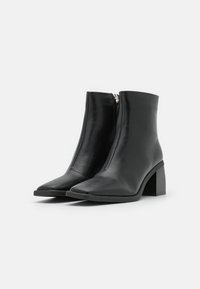 Bottines noires avec une finition en cuir lisse, bout pointu, dotées d'une fermeture éclair sur le côté et d'un talon bloc pour plus de stabilité.