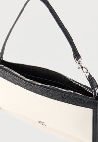 Μαύρη και λευκή ορθογώνια τσάντα χειρός με υφή από μαύρο δερμάτινο περίβλημα, ασημένιο φερμουάρ που ανοίγει για να αποκαλύψει το μαύρο εσωτερικό και ένα μόνο μαύρο λουράκι.