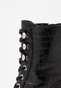 Czarne botki ankle wykonane z sztucznej skóry, z teksturą krokodyla, srebrnymi oczkami i czarnymi sznurowadłami, charakteryzujące się solidną konstrukcją i wyraźnym kształtem.