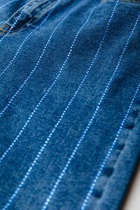 Tejido de denim con rayas verticales azules, con pequeños adornos a lo largo de las líneas. Corte clásico con costuras estándar y bolsillos.