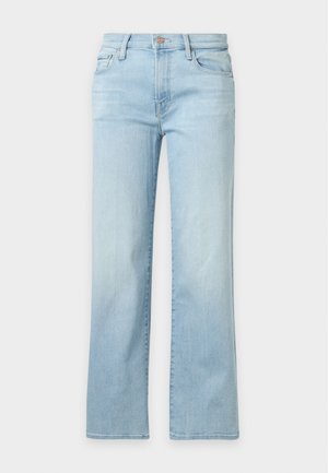 Kvinde stående iført en mørkeblå langærmet trøje, lyseblå jeans med lige ben og sorte ankelstøvler på hvid baggrund.