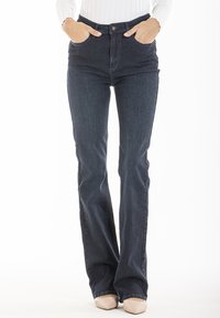 Jeans évasés de couleur bleu foncé en denim, taille haute, avec des poches avant, un bouton en métal et une braguette zippée. Tissu texturé visible.