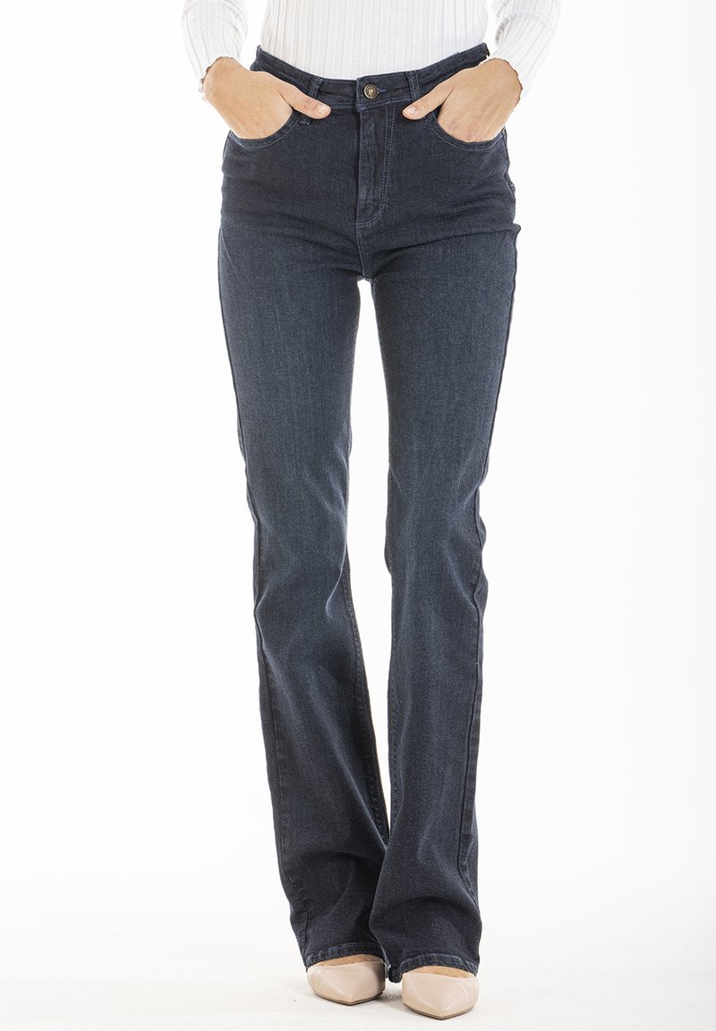 Jeans évasés de couleur bleu foncé en denim, taille haute, avec des poches avant, un bouton en métal et une braguette zippée. Tissu texturé visible.