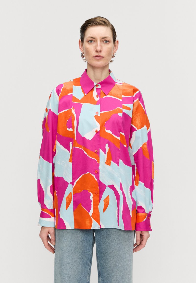Multicolored button-up shirt features bold pink, orange, and light blue abstract patterns. Long sleeves, collar, and relaxed fit design.