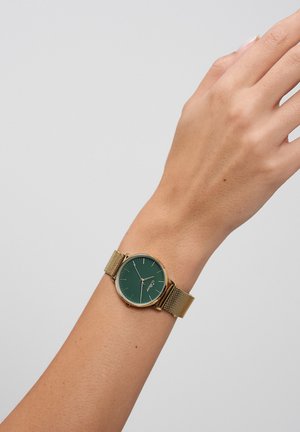 Runde Uhr mit grünem Zifferblatt und goldenen Stundenmarkierungen. Goldenes Mesh-Armband. Glatter, glänzender Zifferblattabschluss.