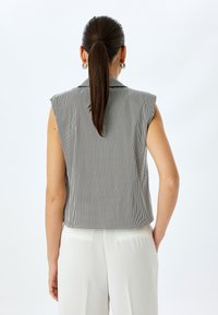 Top senza maniche con righe verticali bianche e nere, caratterizzato da un design con colletto e una vestibilità relaxed, abbinato a pantaloni di colore chiaro.