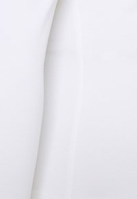 Valkoinen kangas, jossa on sileä pinta, hienovarainen kiilto ja venyvyys. Materiaali vaikuttaa kevyeltä ja on ryppyjemätä.