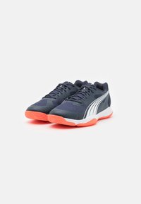 Baskets de sport navy avec tige en mesh, accents blancs et semelle extérieure orange vif. Comprend des lacets et une adhérence texturée sur la semelle.