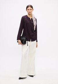 Langärmlige, dunkelviolette Bluse mit gerafftem Ausschnitt, kombiniert mit weißen, ausgestellten Hosen. Accessories: schwarze gefaltete Handtasche und gemusterter Schal.