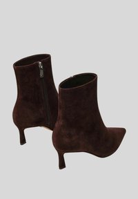 Stivaletti in suede marrone alla caviglia con punte appuntite, tacco slim di 5 cm e zip laterali per una facile calzata. Texture liscia e silhouette elegante.