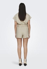 Combinaison en lin beige au design décontracté, avec des manches courtes et une taille élastique. Associée à des bottes beiges arrivant à la cheville avec des talons larges.