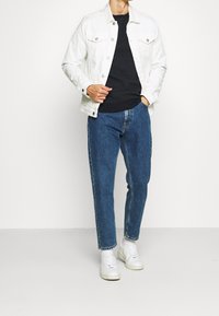 Weiße Jeansjacke über einem schwarzen strukturierten Pullover, kombiniert mit hellblauen, geraden Jeans und weißen Sneakers. Schlichtes und modernes Design.