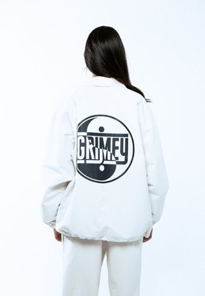 Chaqueta blanca de gran tamaño con un gráfico yin-yang negro y la palabra "GRIMEY" centrada en la parte posterior, con una textura suave y mate.