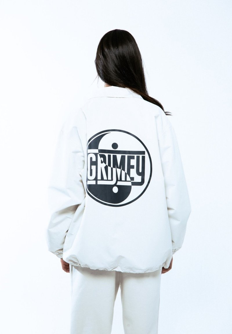 Biała, oversize'owa kurtka z czarnym graphic yin-yang i napisem "GRIMEY" umieszczonym na środku pleców, charakteryzująca się gładką, matową teksturą.