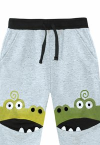 Pantaloni jogger grigi con vita nera, caratterizzati da volti di mostro verdi sulle tasche frontali. Il materiale ha una texture maculata. Inclusi i lacci.