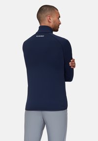Marineblauwe coltrui met lange mouwen en rits, gemaakt van een gladde stof. Beschikt over een logo op de achterkant van de nek en platte naden voor comfort.