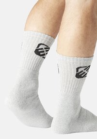 Chaussettes en coton gris avec une texture côtelée, arborant un logo noir près du haut. Les chaussettes couvrent la cheville et offrent un ajustement serré.
