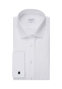 Chemise habillée blanche ajustée pliée avec col large et bouton de manchette noir sur le poignet gauche, sur fond blanc.