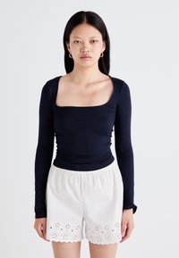 Haut à manches longues bleu marine avec un décolleté carré, design ajusté, associé à un short blanc avec des détails en œillet le long de l'ourlet.