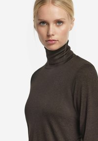 Brun polotröja i mjukt tyg. Har en figursydd design med fina sömmar längs halsen och axlarna.