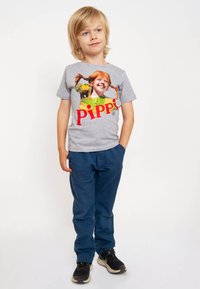 Gray t-shirt featuring a colorful print of a character with red hair, paired with blue trousers and black shoes with a white sole.