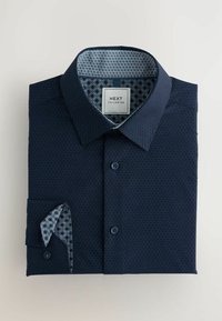 Marineblauw overhemd met knopen en een textuurpatroon, contrasterende gekleurde kraagvoering en bijpassend manchetdetail. Opgevouwen met een zak.