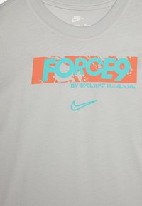 Grå kortärmad T-shirt med rundad hals, med en iögonfallande grafisk design i orange och aqua som säger "FORCE9" samt en liten Nike-logotyp.