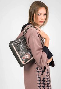 Bolso negro con un diseño gráfico que presenta a una chica y monumentos, decorado con un asa de cadena trenzada plateada y múltiples acentos.