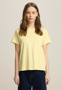 Żółta bawełniana koszulka z okrągłym dekoltem, krótkimi rękawami i luźnym krojem. Charakteryzuje się gładką fakturą i minimalistycznym designem.
