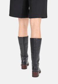 Bottes en cuir noir montantes, avec une texture lisse, un bout rond et un talon en bois empilé, vues de l'arrière.