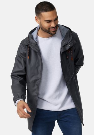 Chaqueta impermeable de color gris oscuro con cierre de cremallera, puños elásticos y capucha. Cuenta con cordones de color naranja y un bolsillo en el pecho con cremallera.