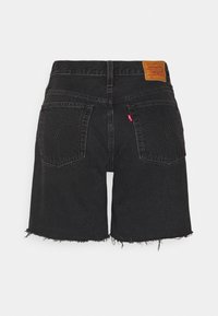 Short en jean noir avec des ourlets effilochés, deux poches arrière, une petite étiquette rouge sur la poche droite, et un patch en cuir marron sur la ceinture.