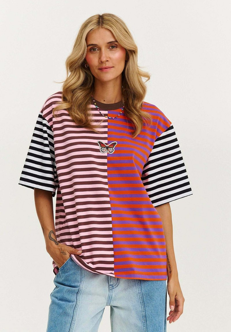 Koszulka oversize w paski, z sekcjami w kolorach różowym, brązowym, pomarańczowym i czarnym. Posiada motyw motyla na przodzie oraz krótkie rękawy.