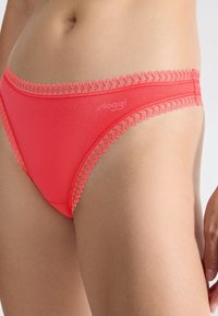 Culottes Sloggi de couleur corail avec un tissu lisse, un délicat bord en dentelle le long de la taille et une coupe classique.