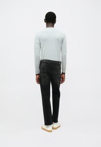 Μαύρο τζιν με ίσια εφαρμογή, ελαφριά φθορά και ταμπέλα στη μέση πίσω. Συνδυασμένο με ανοιχτό γκρι μακρυμάνικο πουκάμισο και λευκά παπούτσια.