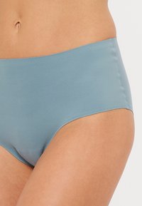 Høy midje truse i lys blått stoff. Myk, glatt tekstur med sømløst design og en beskjeden cut langs benåpningene.