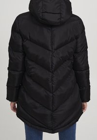 Sort dunjakke med hætte, med et chevron-quiltet mønster, glat tekstur og en kant, der buer i bunden.