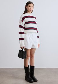 Χοντρό πλεκτό πουλόβερ σε λευκό με κόκκινες και ναυτικές ρίγες; συνδυασμένο με λευκά σορτς με ψηλή μέση και μαύρες μπότες πάνω από το γόνατο με χοντρό τακούνι.