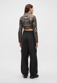 Μέταλλικό κοντό μπουφάν με μακριά μανίκια και ραμμένες λεπτομέρειες, σε συνδυασμό με φαρδιά μαύρη φόρμα cargo. Ομαλή υφή και εμφανείς πρακτικές τσέπες.