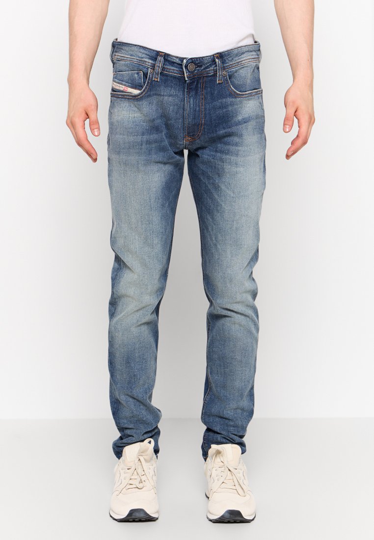 Jeans in denim blu con lavaggio sbiadito, cinque tasche e chiusura con bottone. Indossati con sneaker beige.