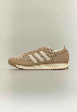 Béžová teniska Adidas s bielymi pruhmi, zvrškom zo semišu a sieťoviny, polstrovanou podrážkou a značkovými detailmi na päte a medzipodrážke.