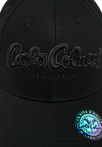 Sort kasket med broderet "Carlo Colucci Milano 1973" logo. Har et cirkulært holografisk mærke. Lavet af glat stof med struktureret top.